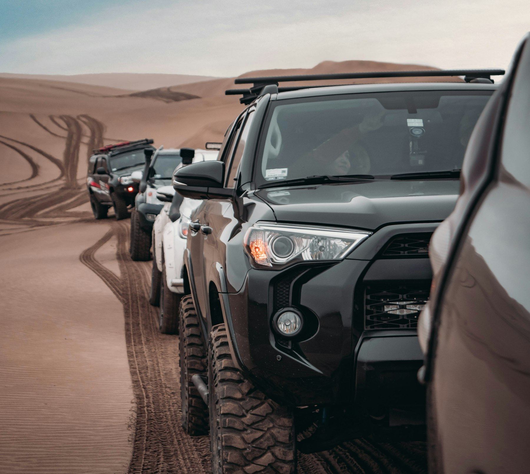 Line of lifted fifth-generation 4Runners on big mud-terrain tires waiting on desert sand dunes