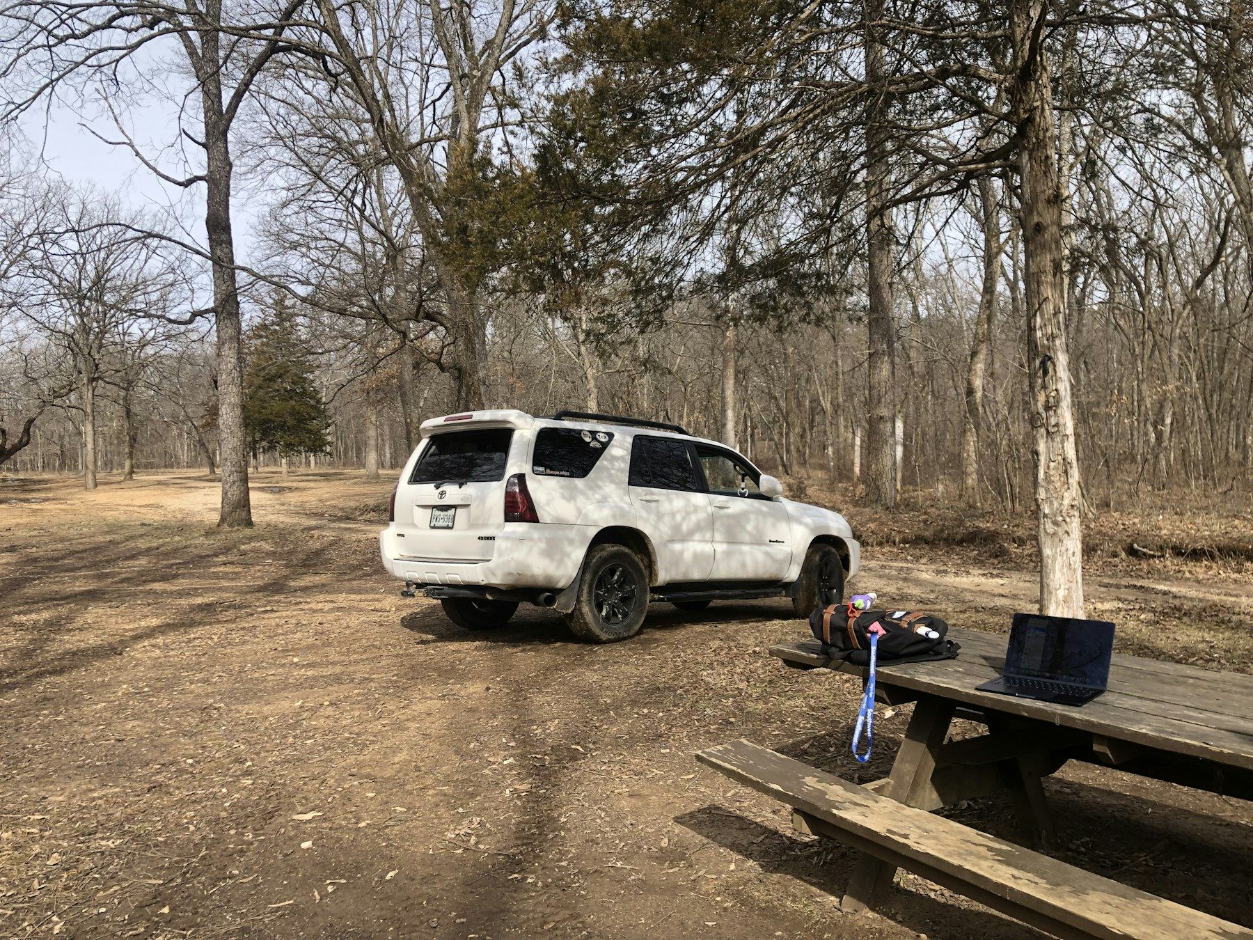 White fourth-generation 4Runner parked at a wooded campsite beside a picnic table
