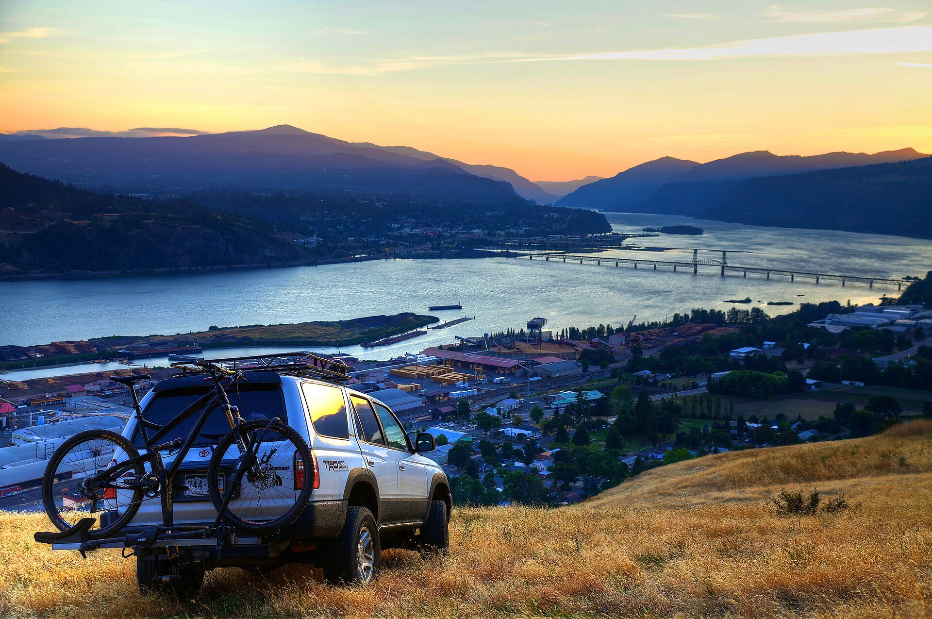 Silver third-generation 4Runner with a mountain bike on its hitch rack parked on a grassy hilltop above the Columbia River at sunset