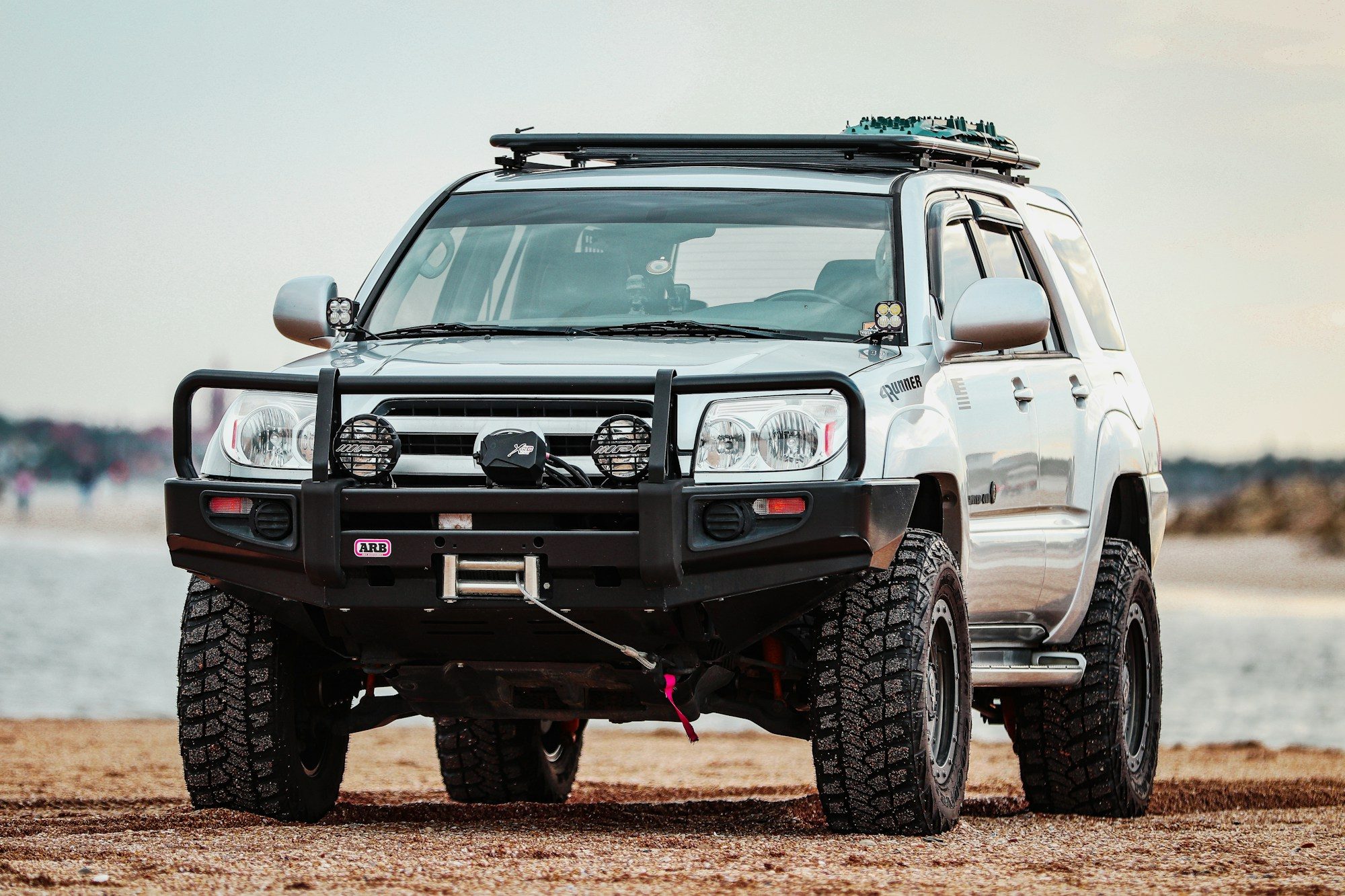 White fourth-generation 4Runner built for overlanding with an ARB steel bumper, winch, driving lights and roof rack on beach sand