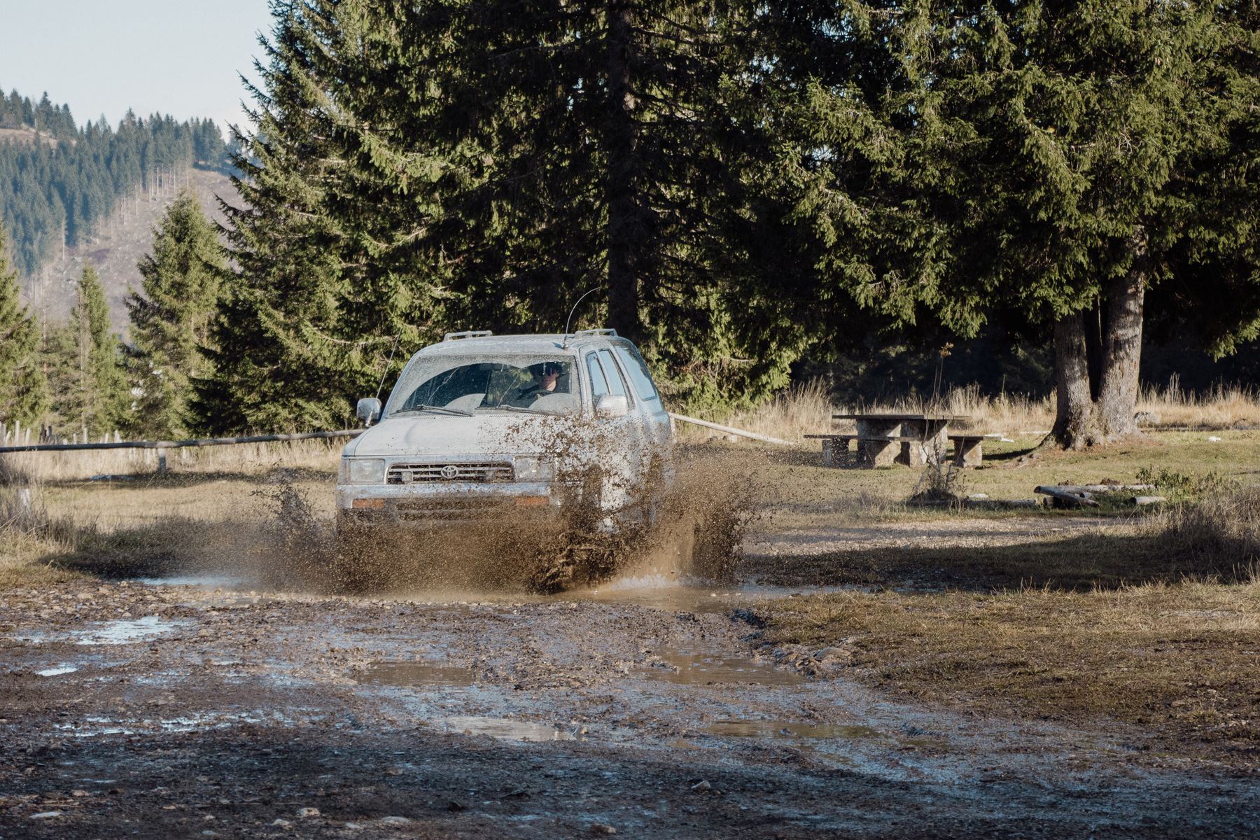 Lifted second-generation 4Runner driving through mud on a forest trail lined with pines