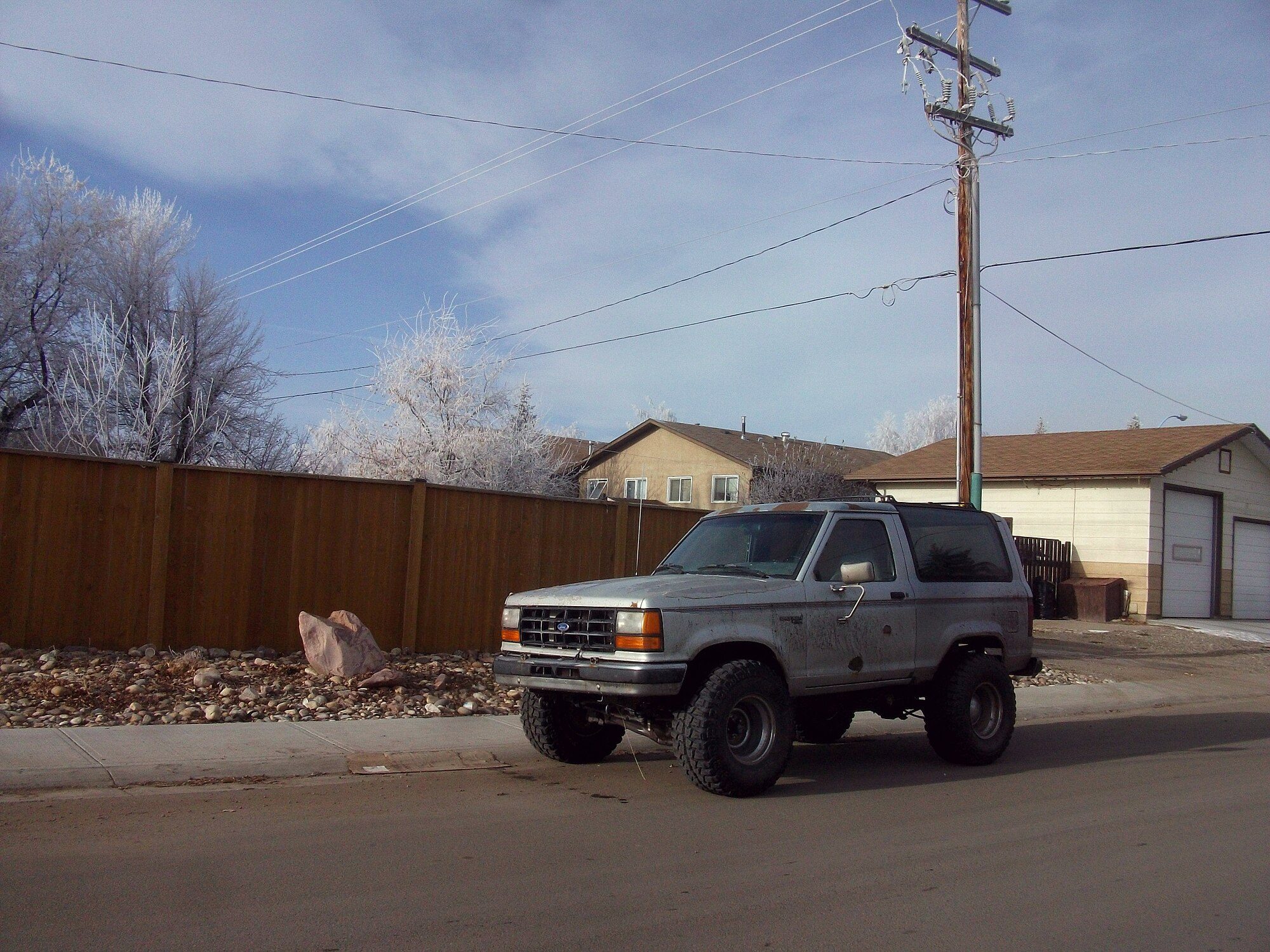 A lifted, dusty silver 1989–90 Ford Bronco II on large mud-terrain tires parked on a frosty winter morning