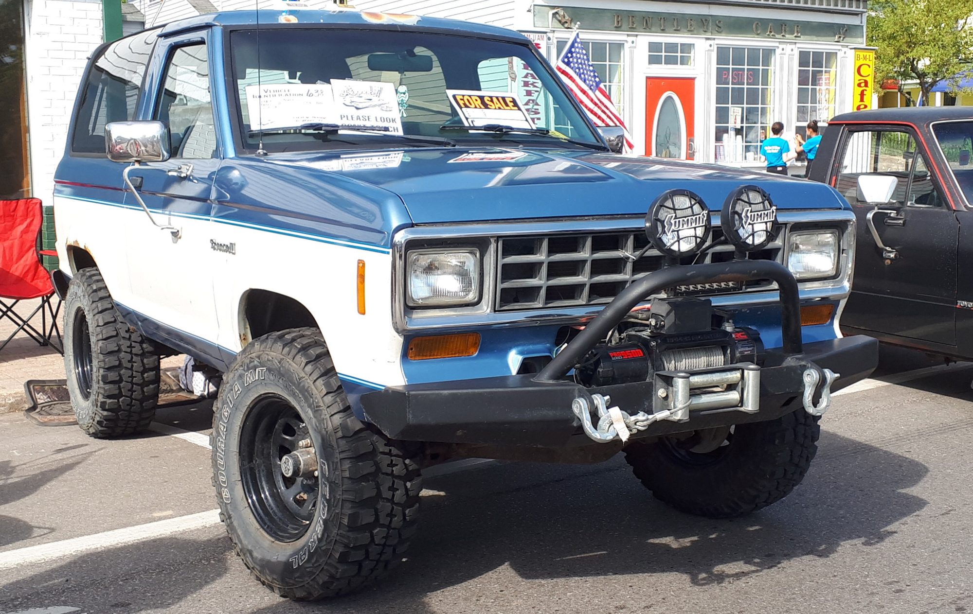 A lifted blue-and-white 1984–88 Ford Bronco II with a winch bumper, off-road lights and mud-terrain tires
