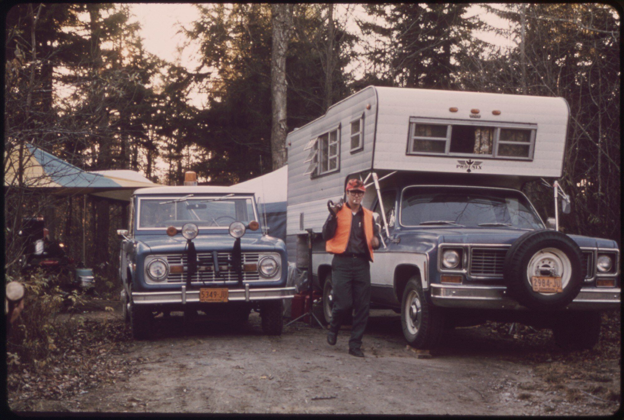 A blue early Ford Bronco with auxiliary lights beside a pickup camper at a hunters' camp on the Moose River Plains, Adirondack Forest Preserve, in the 1970s