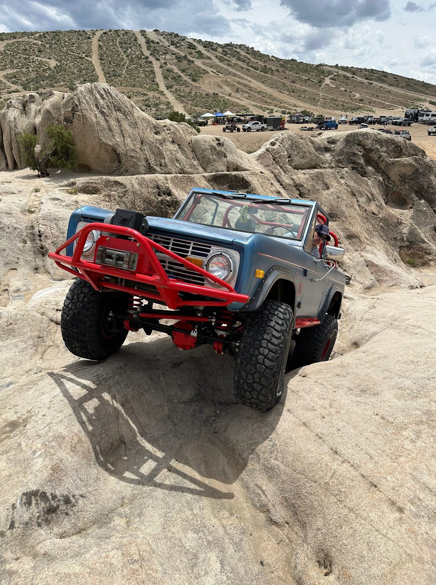 A blue early Ford Bronco with a red tube bumper climbing a sandstone ledge at Moon Rocks OHV Area