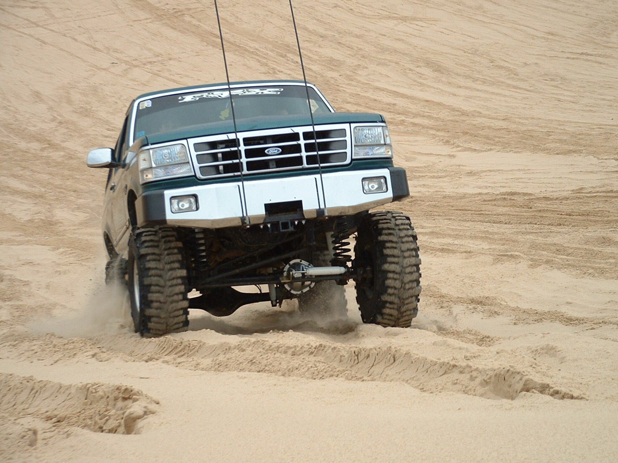 A lifted green-and-white 1992–96 Ford Bronco with a bull bar climbing a sand dune
