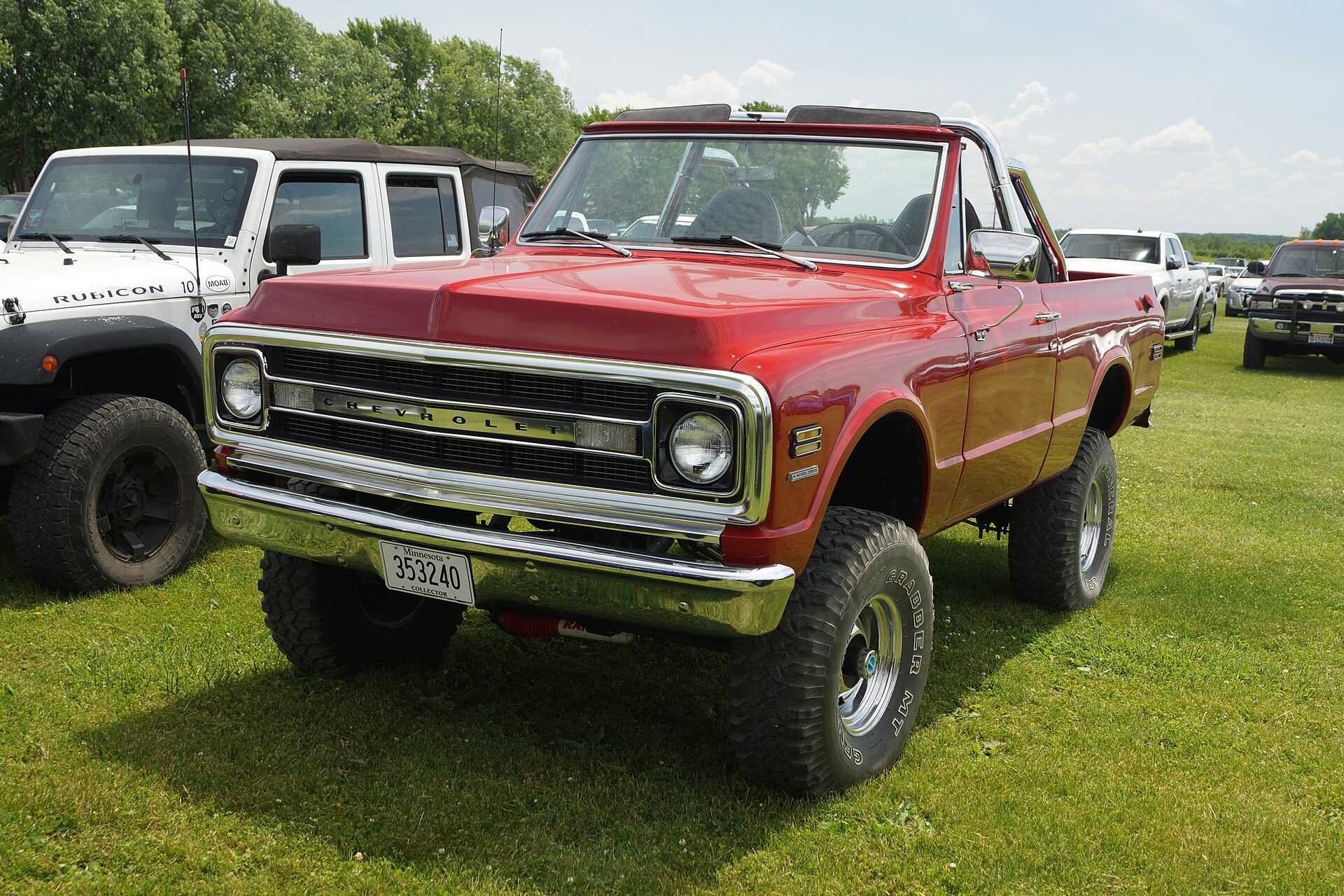 A red, lifted 1970 Chevrolet K5 Blazer with its top off, parked on grass at a Minnesota show field