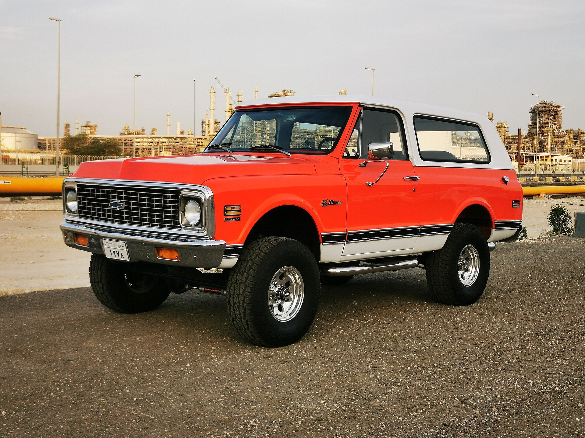 An orange 1971–72 Chevrolet K5 Blazer with a white hardtop and egg-crate grille on a gravel lot in Bahrain
