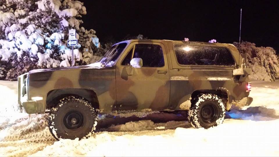 A camouflaged M1009 CUCV Blazer on big tires parked in deep snow at night