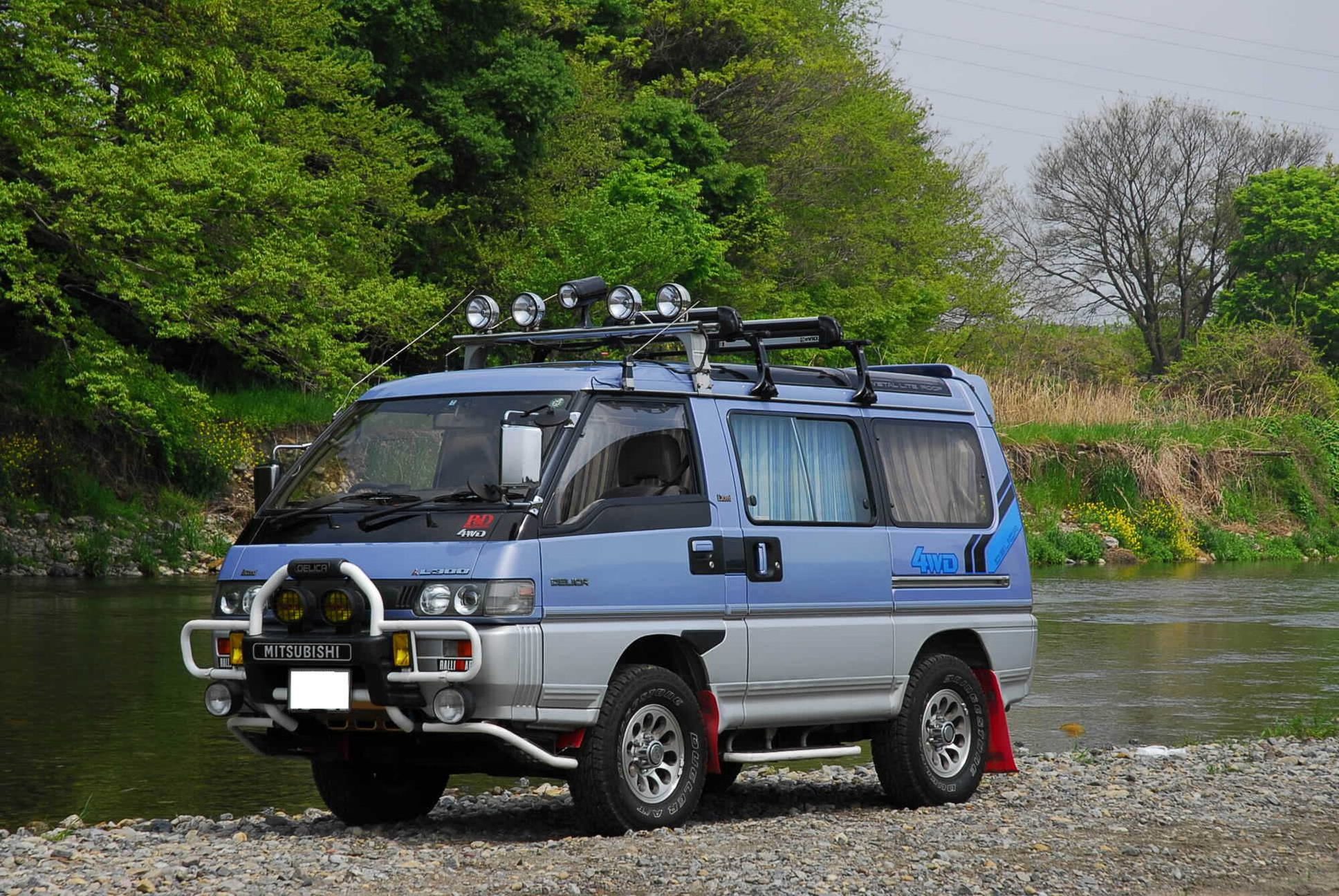 A blue and silver Delica Star Wagon Exceed 4WD with Crystal Lite Roof, roof lights and a bull bar parked on a gravel riverbank in Japan