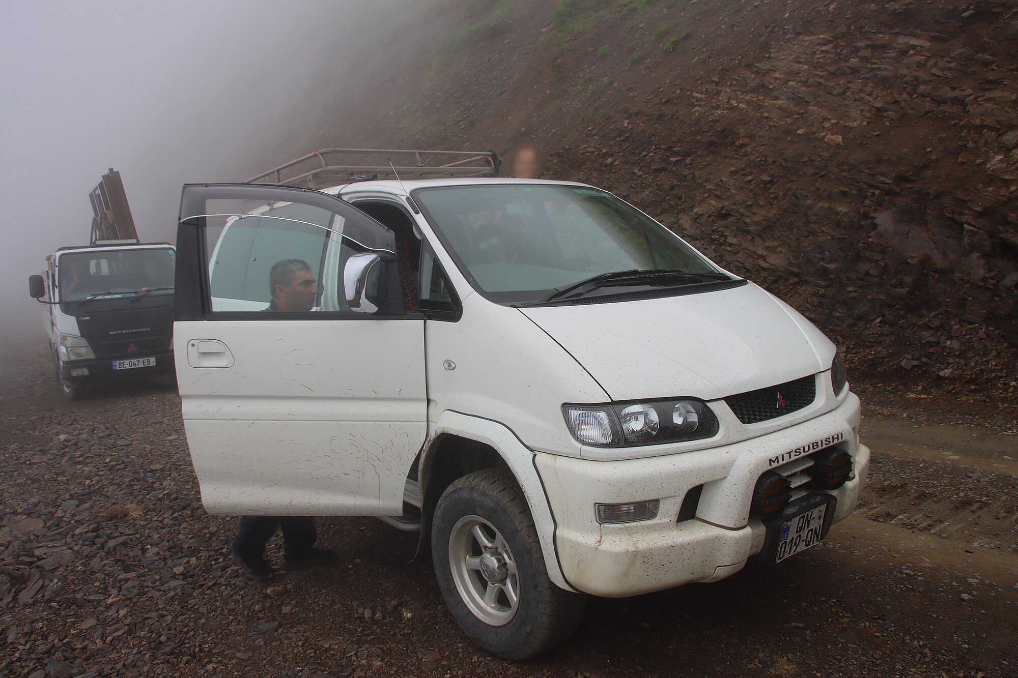 A white Series 2 Delica Space Gear with a roof rack and auxiliary lights stopped on a muddy gravel track on the fog-bound Abano Pass in Georgia