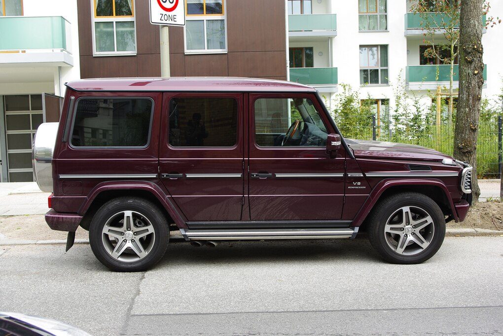 A maroon G 55 AMG Kompressor (V8 Kompressor wing badge) in side profile parked on a city street