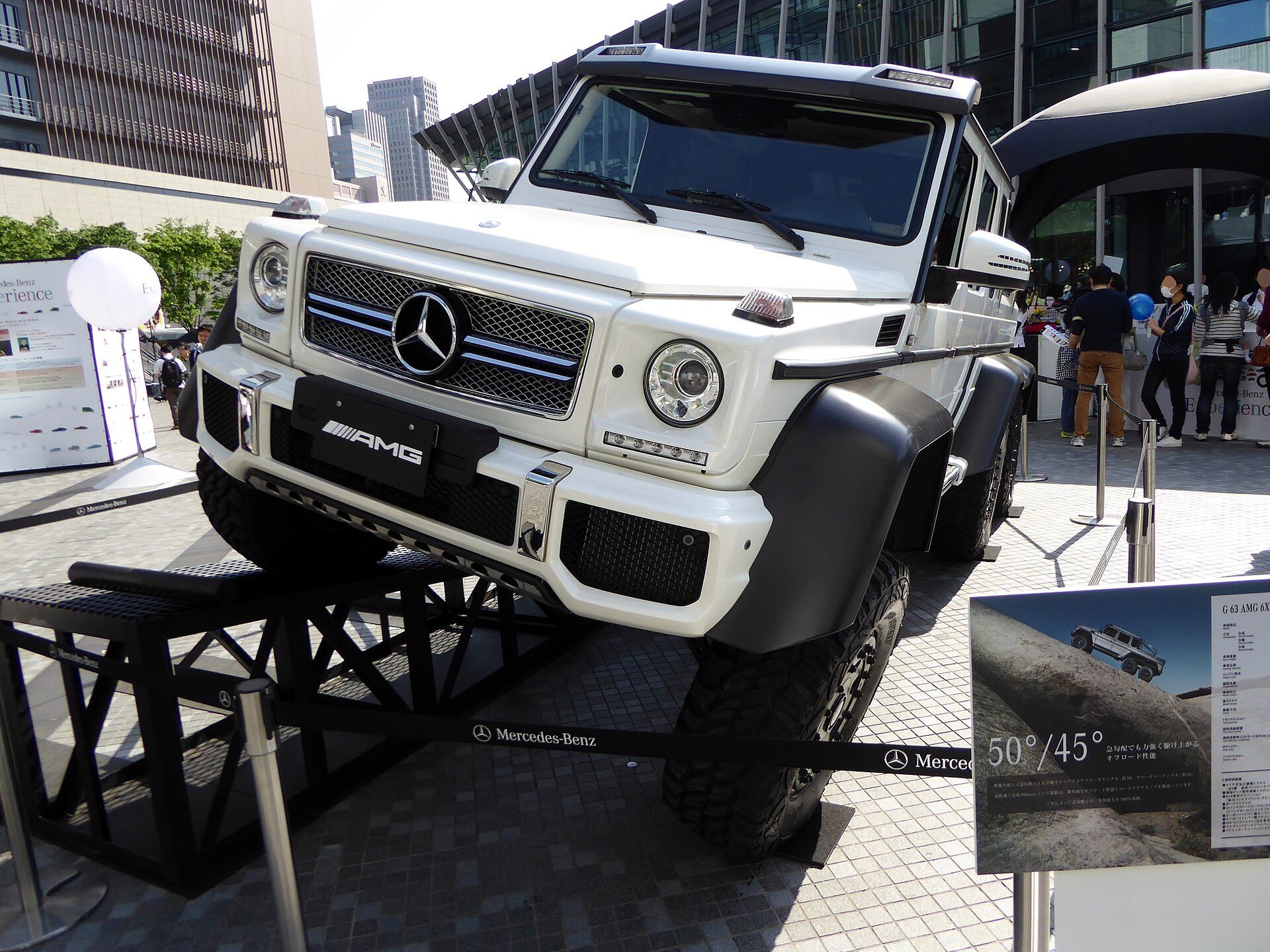 A white G 63 AMG 6×6 climbing a steel display ramp beside a sign quoting 50° and 45° approach and departure angles