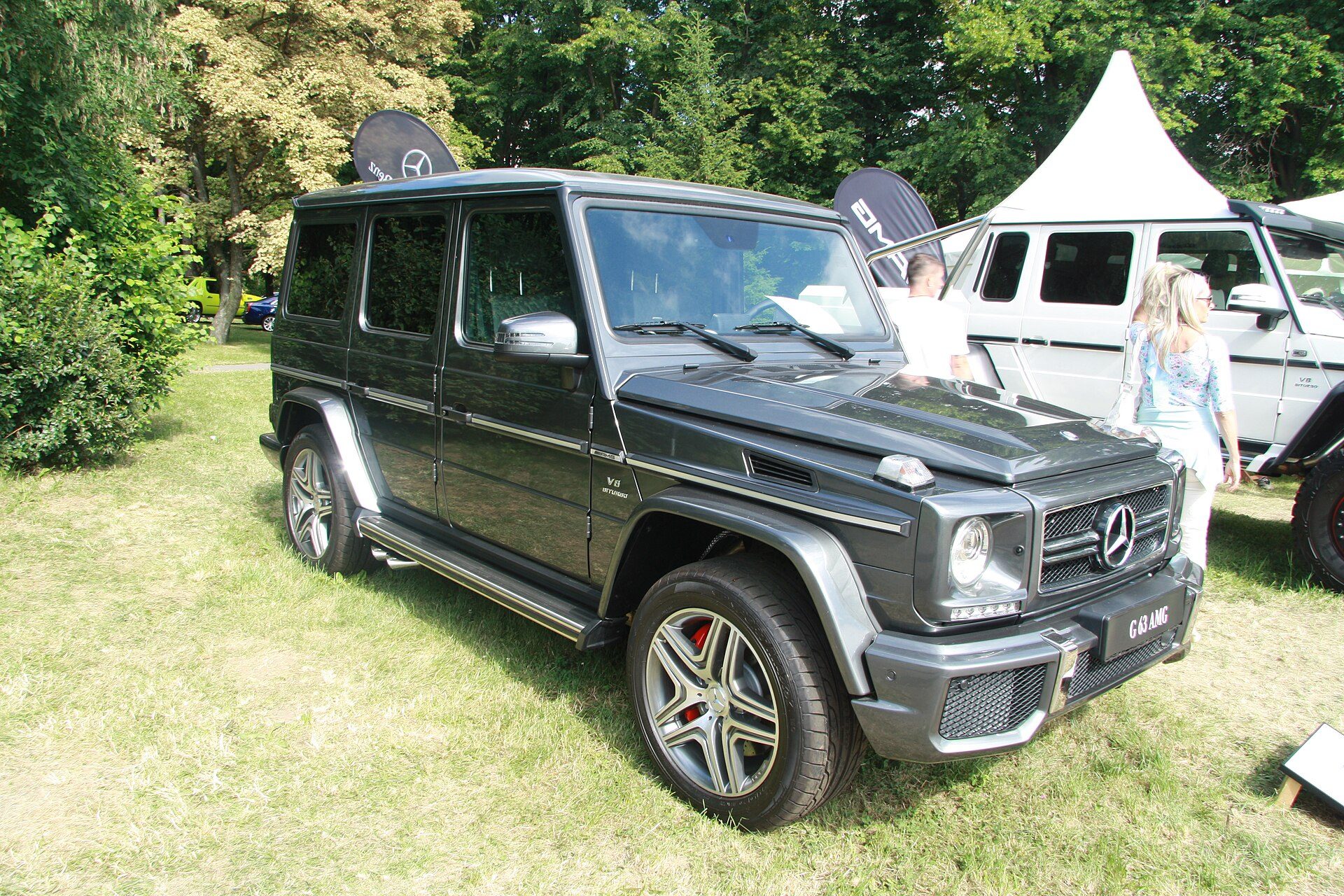 A dark grey G 63 AMG with V8 Biturbo fender badges parked on grass at an outdoor show