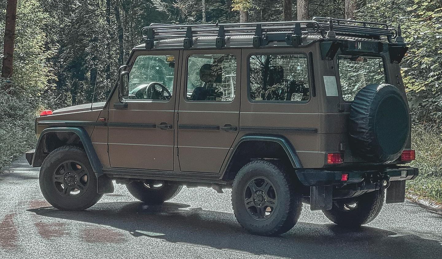 A brown Swiss Army W461 G 300 CDI long-wheelbase wagon with roof rack on a forest track
