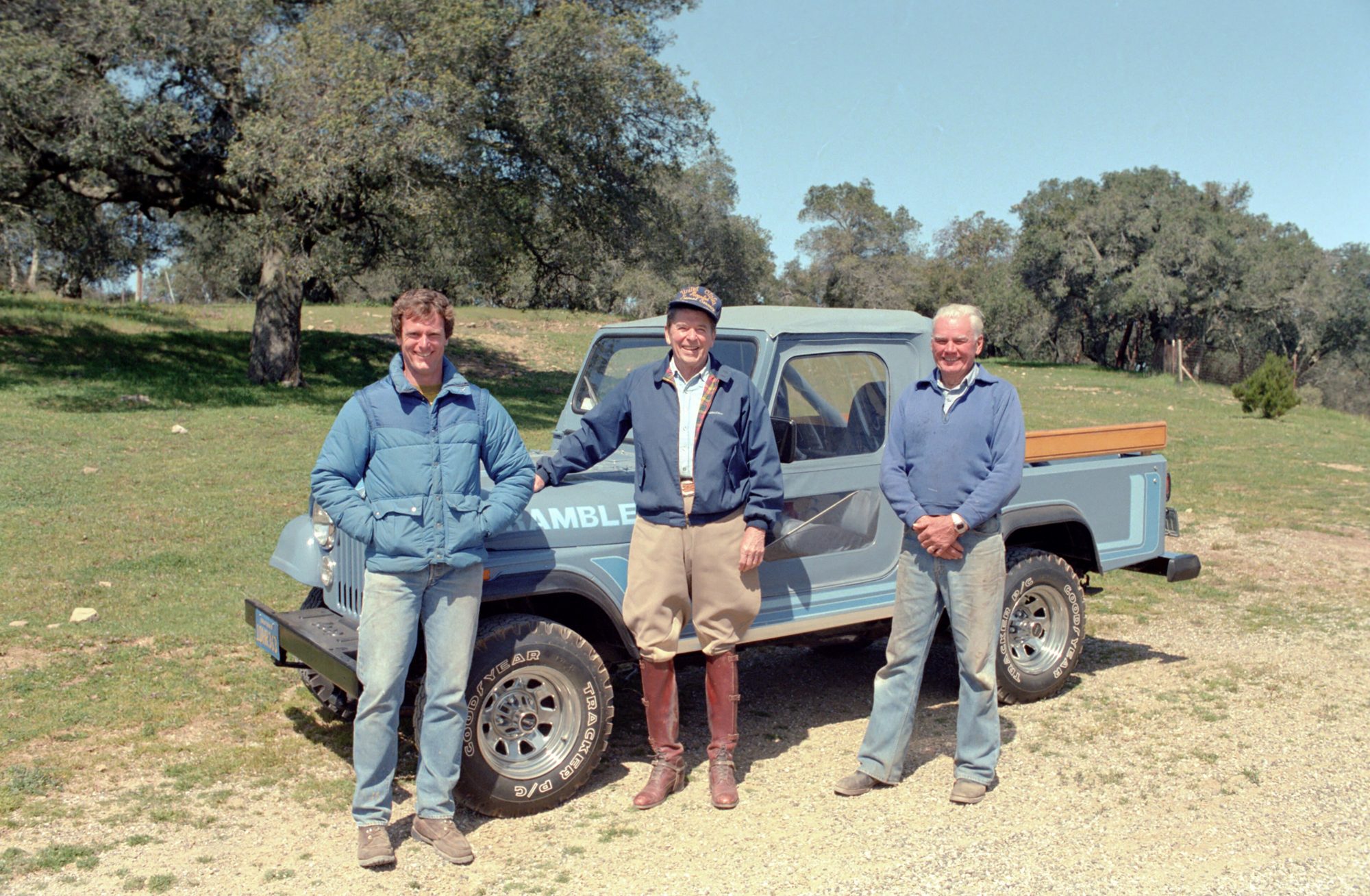 President Ronald Reagan and two ranch hands standing beside his blue Jeep CJ-8 Scrambler, fitted with a soft half cab, in a grassy oak meadow at Rancho del Cielo, 1983