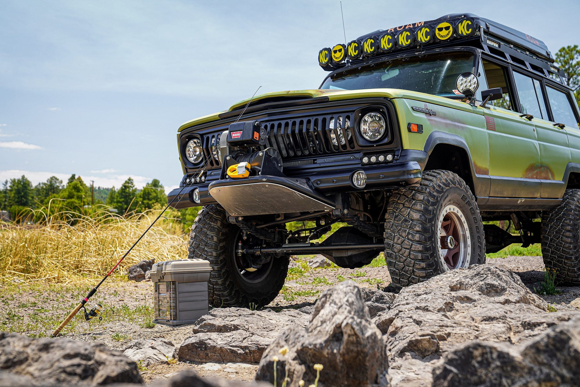 A lifted green 1969 Jeep Wagoneer with a light bar parked on volcanic rock, the earlier SJ that the Grand Wagoneer grew from