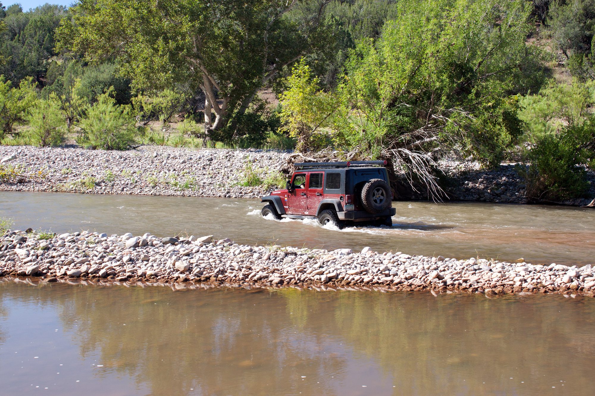 A red Jeep Wrangler JK Unlimited fording the shallow upper Salt River between gravel bars