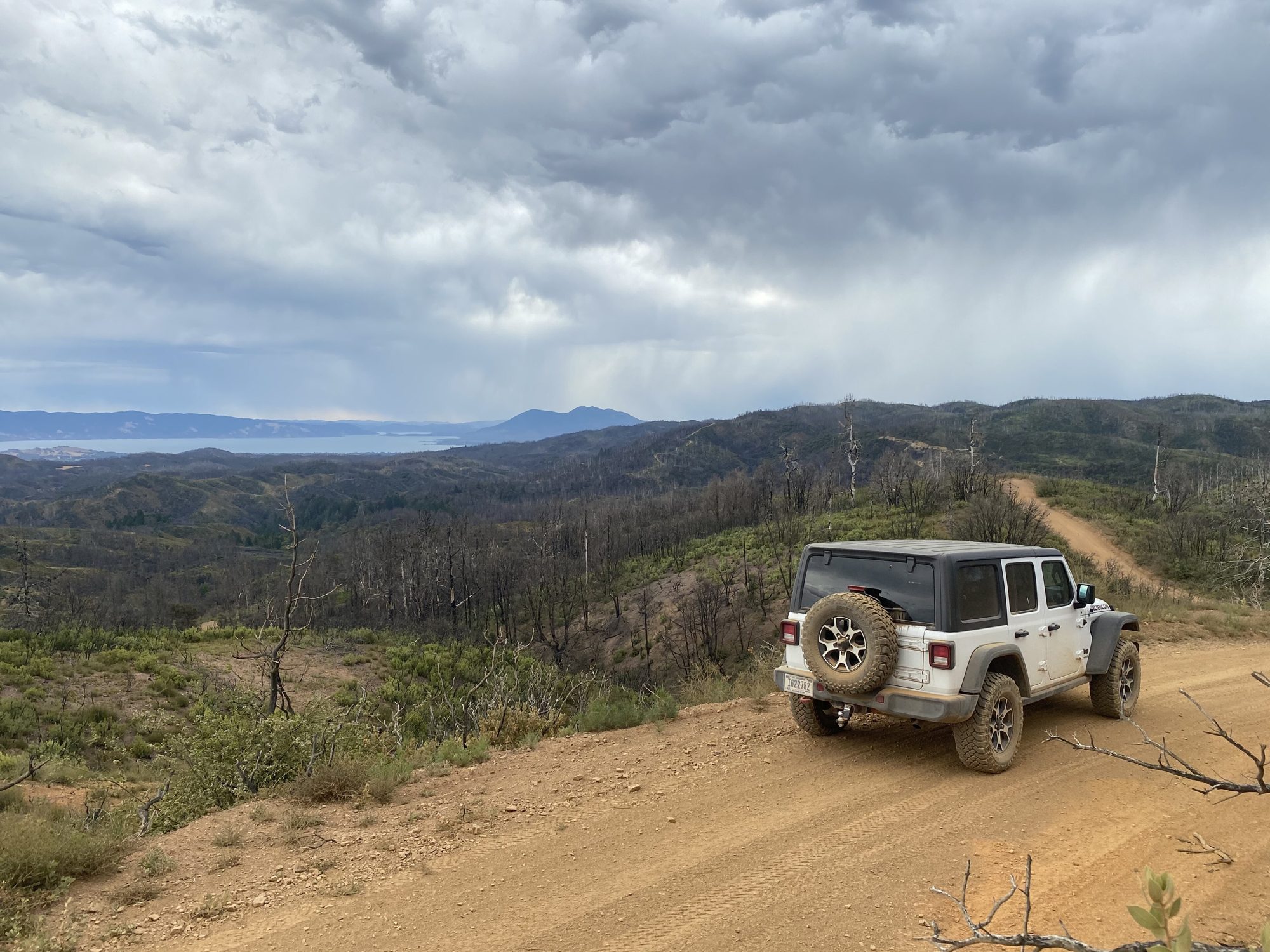 Rear view of a white Jeep Wrangler JL Unlimited on a dirt road on a ridge above Clear Lake, California