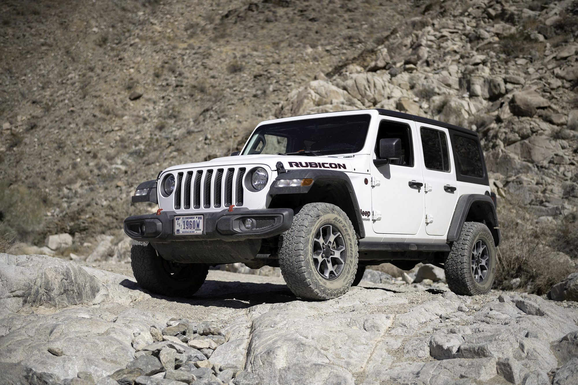 A white Jeep Wrangler JL Unlimited Rubicon crawling down a rocky ledge in a desert wash in Joshua Tree National Park