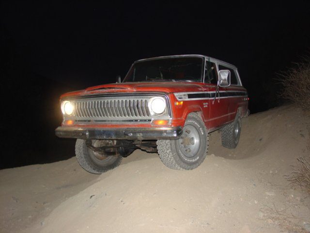 The red two-door Cherokee S with its headlights on, cresting a dirt mound at night