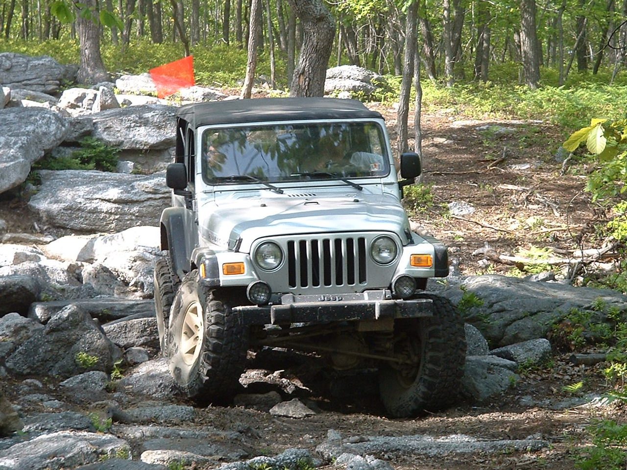 A silver Jeep Wrangler TJ, described by the photographer as a Rubicon, crawling over boulders in the woods