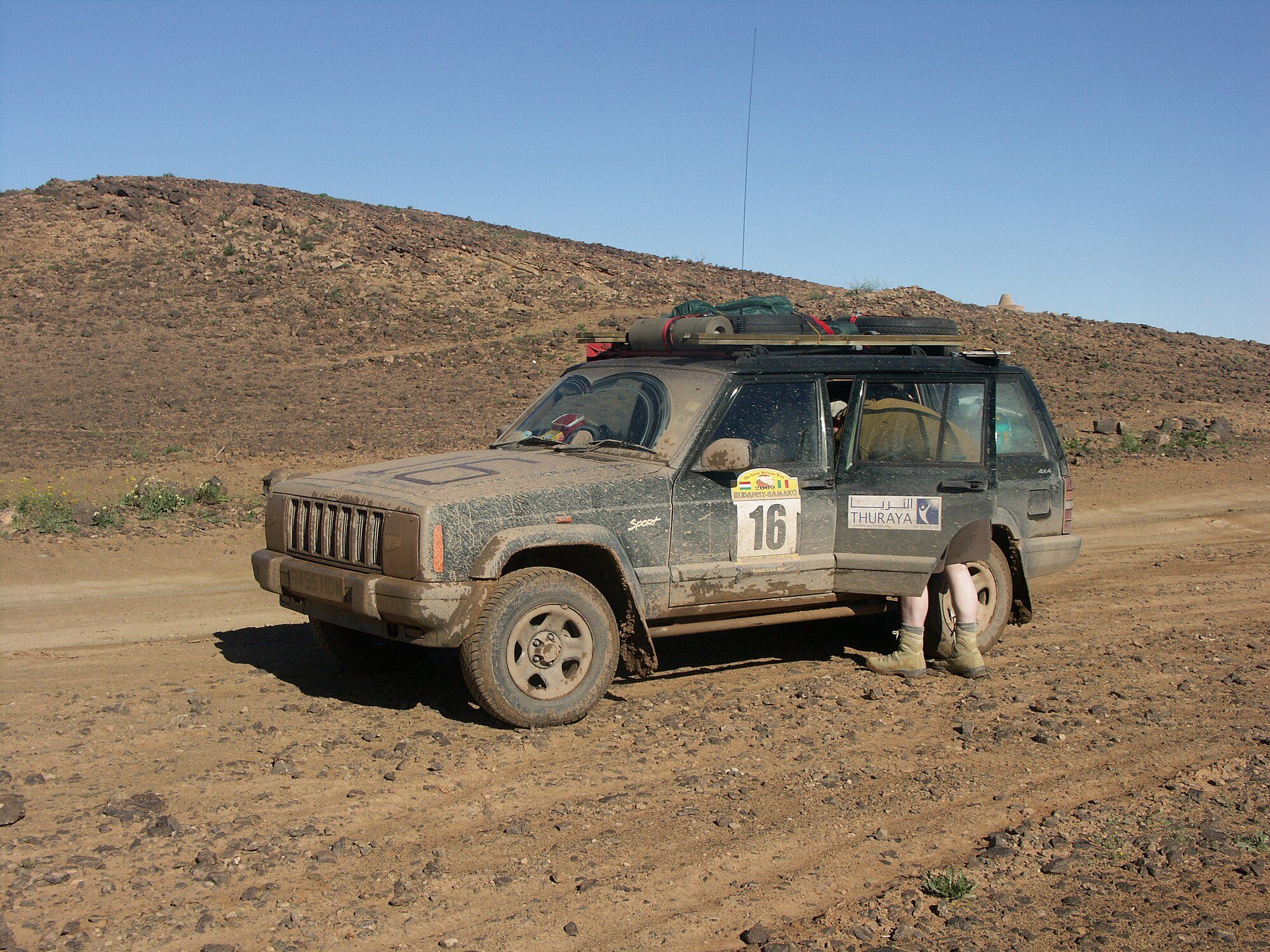 A mud-caked Cherokee XJ with rally number decals on a dirt track in the Moroccan desert