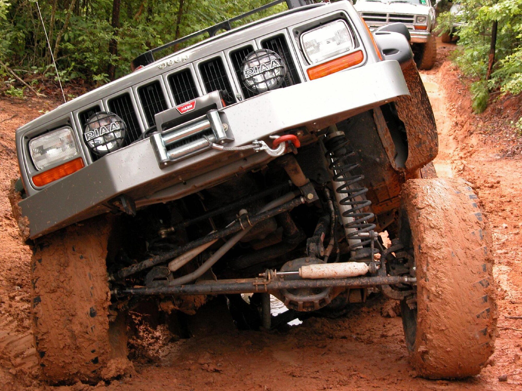 A lifted silver Cherokee XJ on mud tires flexing its front axle in red clay