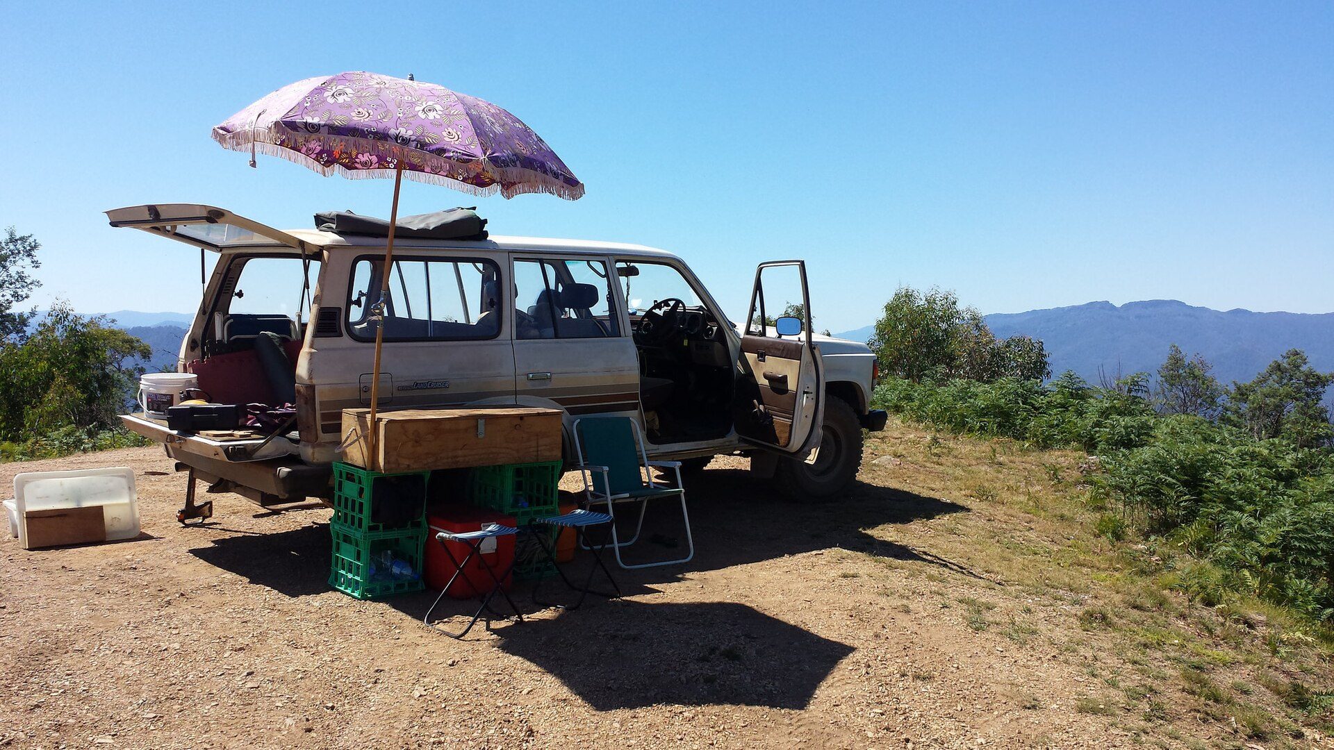 The same 60 Series wagon with doors open and a lunch table and umbrella set up on a ridge-top dirt track