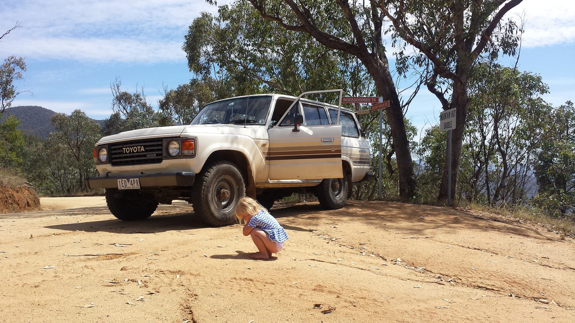 A beige round-headlight Land Cruiser 60 Series diesel wagon parked at a dirt track junction in the Australian high country