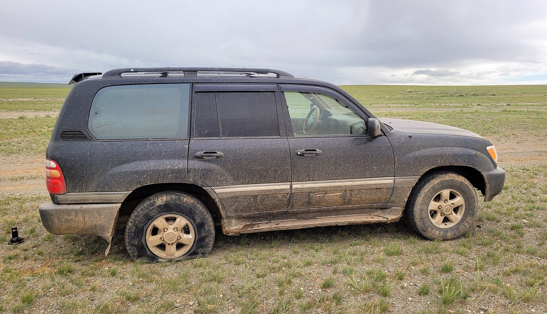 A mud-spattered dark grey Land Cruiser 100 Series parked on the open Mongolian steppe