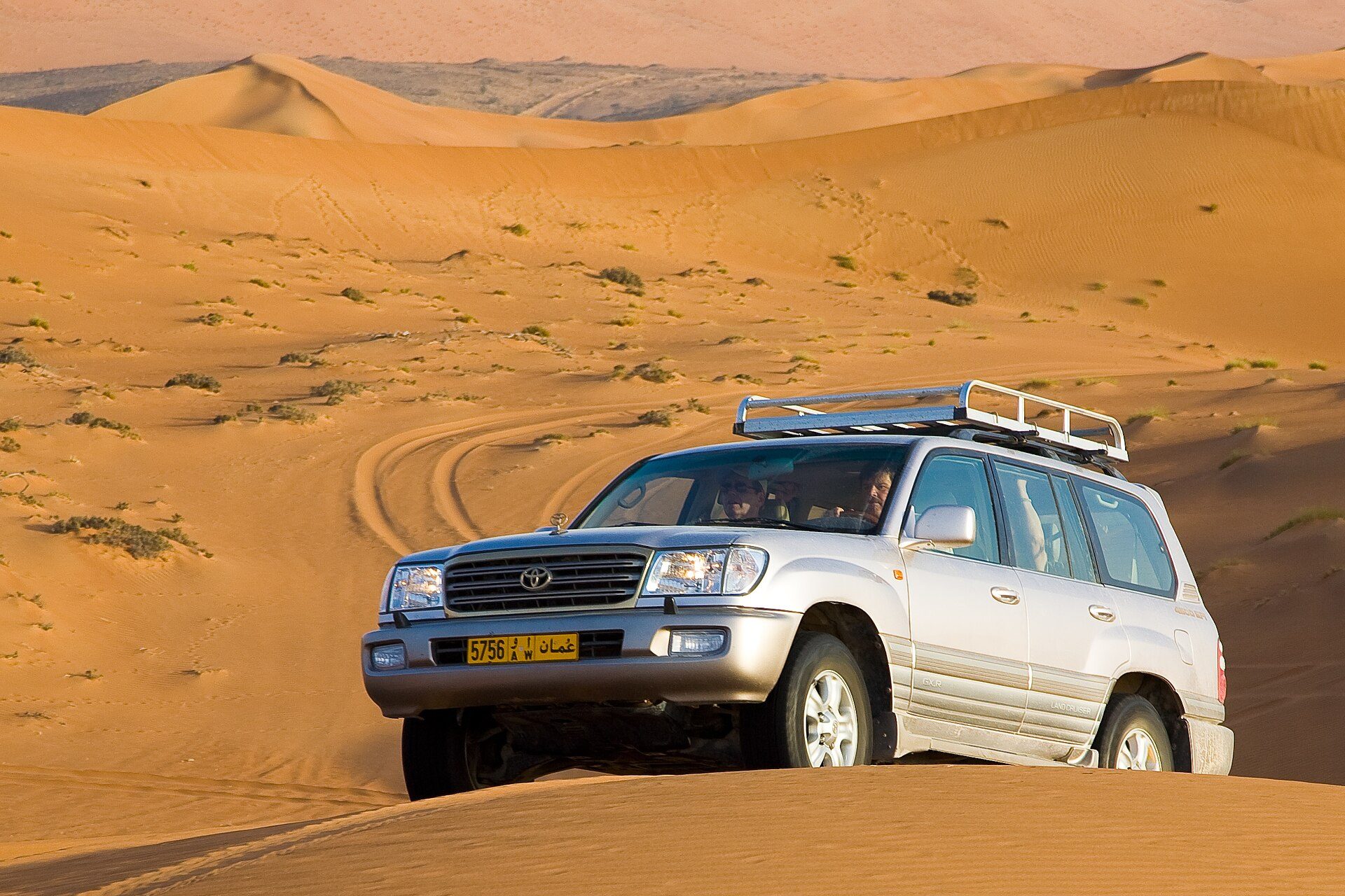 A silver Land Cruiser 100 Series with a roof rack cresting a dune in Oman's Wahiba Sands