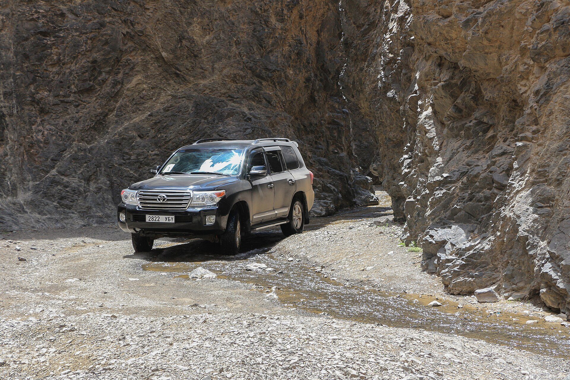 A black Land Cruiser 200 Series driving a gravel track through the rock walls of Dungenee Canyon in Mongolia's Gobi
