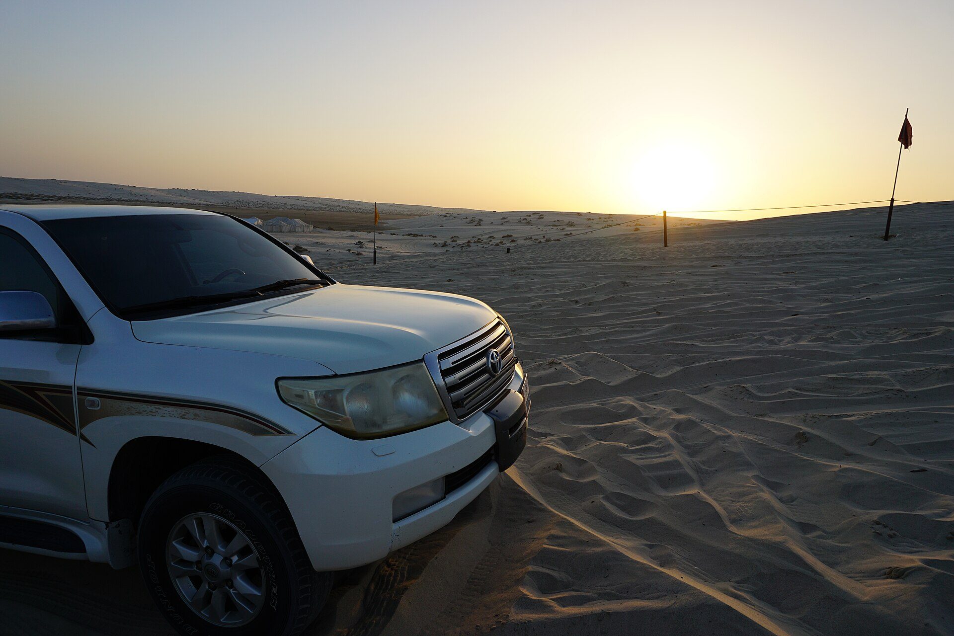 A white Land Cruiser 200 Series parked on rippled sand in the Qatari desert at sunset