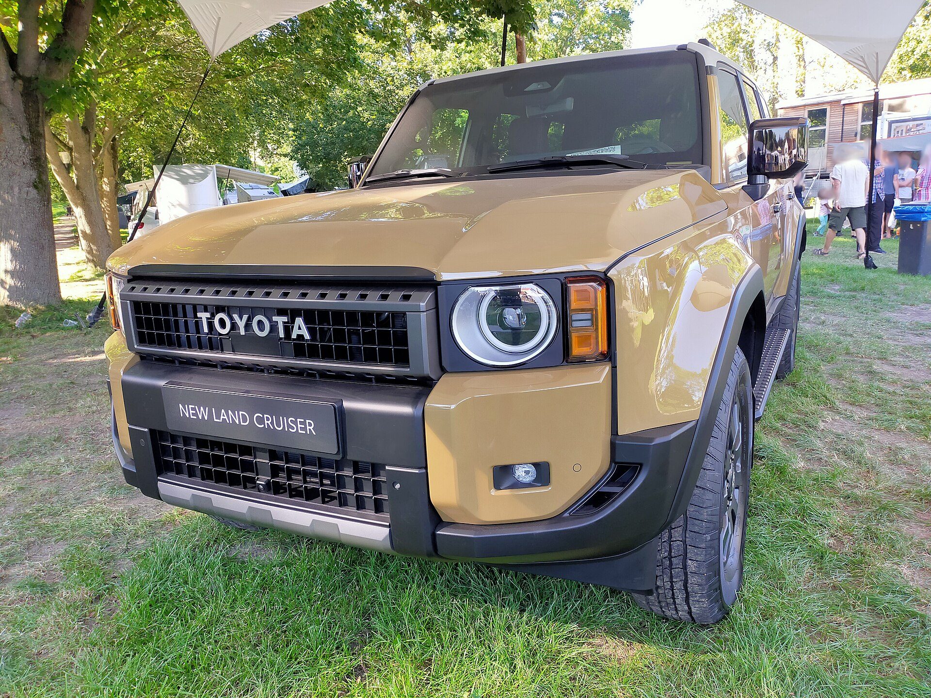 A sand-coloured 250 Series Land Cruiser with round headlights parked on grass at an outdoor display