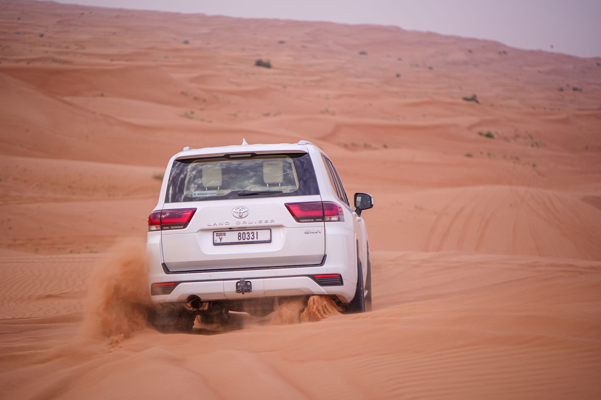 Rear view of the same white 300 Series Land Cruiser GXR spraying sand as it climbs through soft dunes