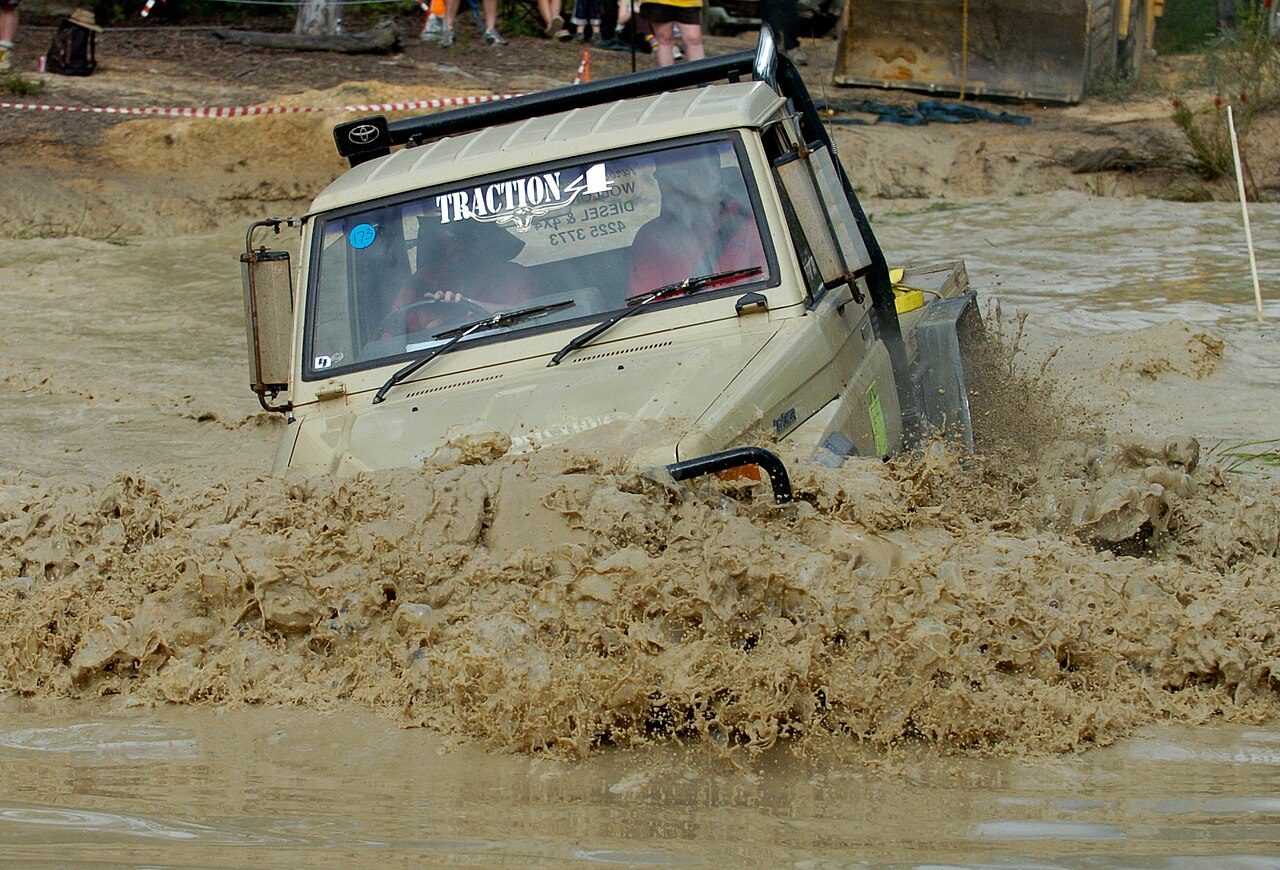 A Land Cruiser 75 Series ute ploughing through a deep mud hole at an Australian 4WD trials competition