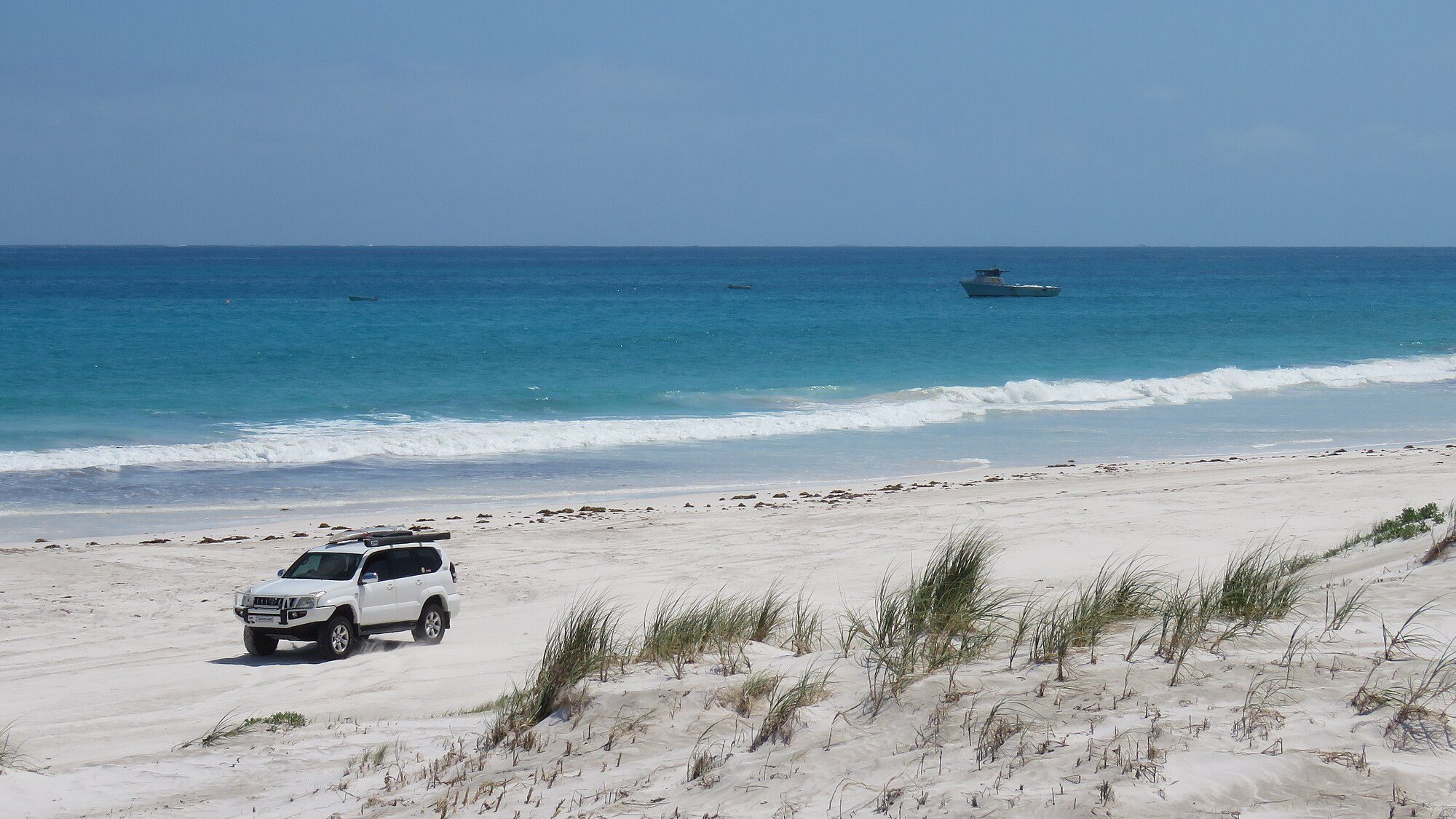 A white Land Cruiser Prado 120 with a roof rack driving along a white-sand beach north of Wedge Island, Western Australia