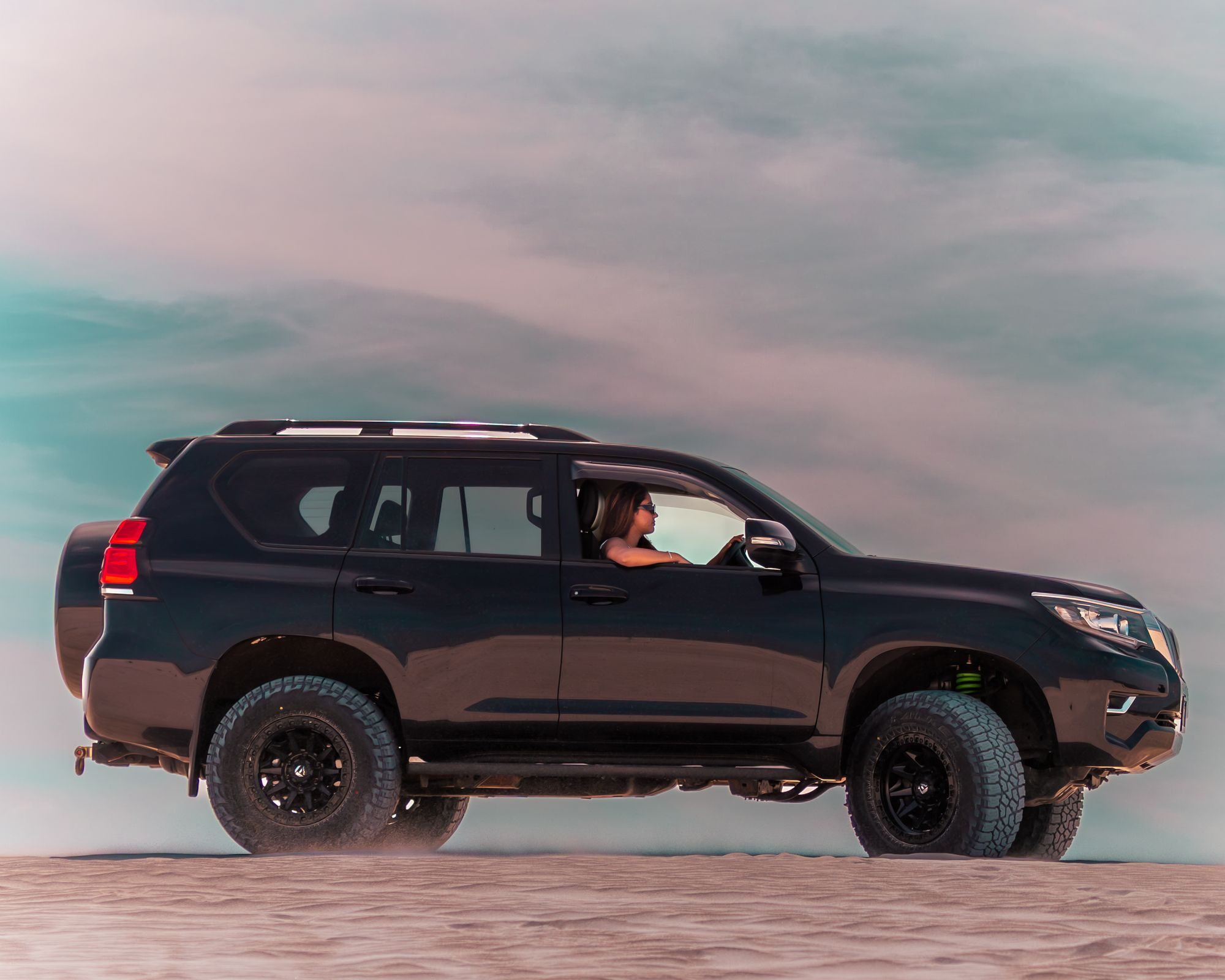 A black, lifted 2017-or-later Toyota Prado 150 on big all-terrain tires driving across a sand dune at Lancelin, Western Australia