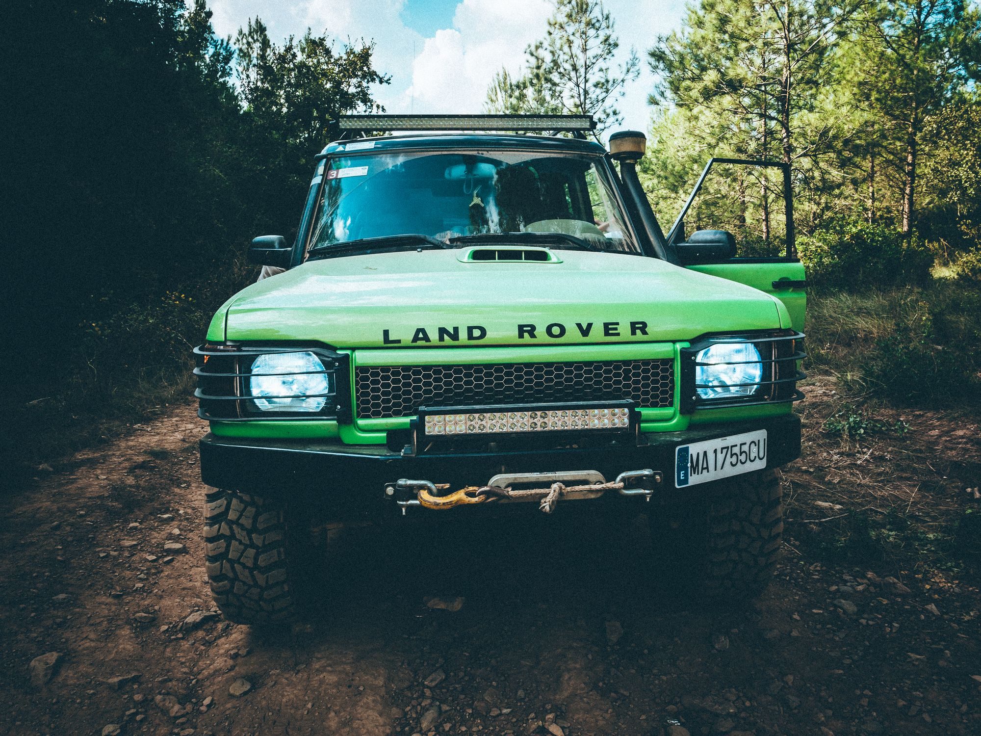 A bright green Discovery Series II with snorkel, winch and light bar on a dirt forest trail