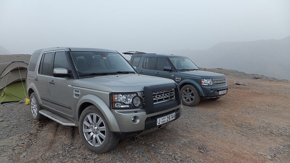 Two Middle East-market LR4s parked on a rocky mountain plateau next to a tent in the haze