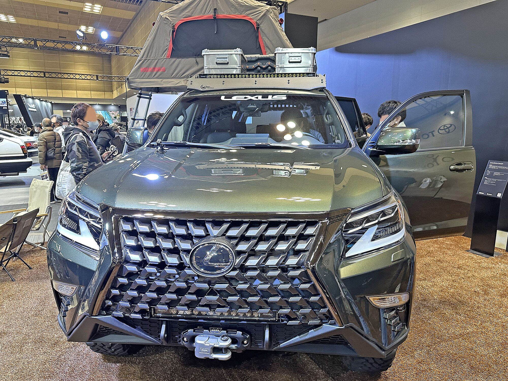 Olive-green Lexus GX Outdoor Concept with a rooftop tent, winch and roof rack on a show stand