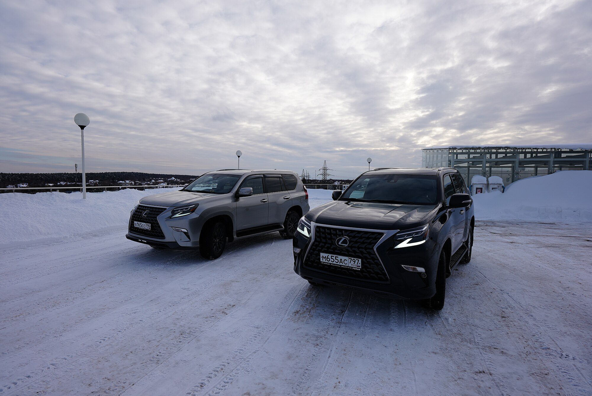 A black and a silver 2020-era Lexus GX 460 parked side by side on a snow-covered lot in Russia