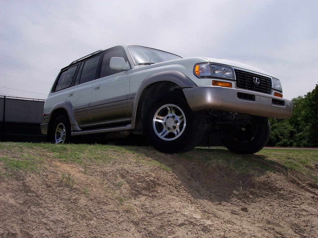 A silver Lexus LX 450 with one front wheel up on a dirt mound