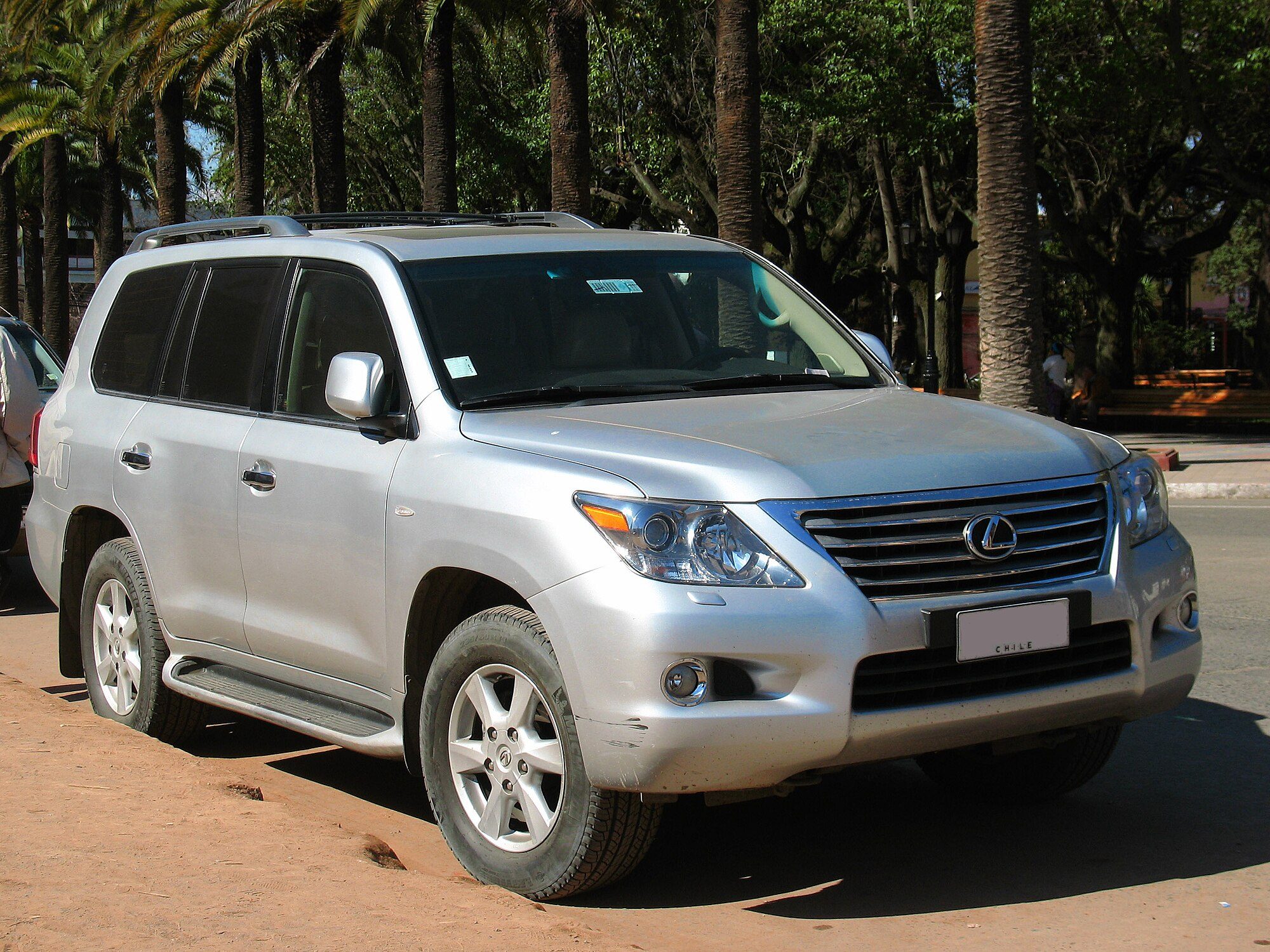 A silver 2009 Lexus LX 570 parked on red dirt under palm trees in Chile