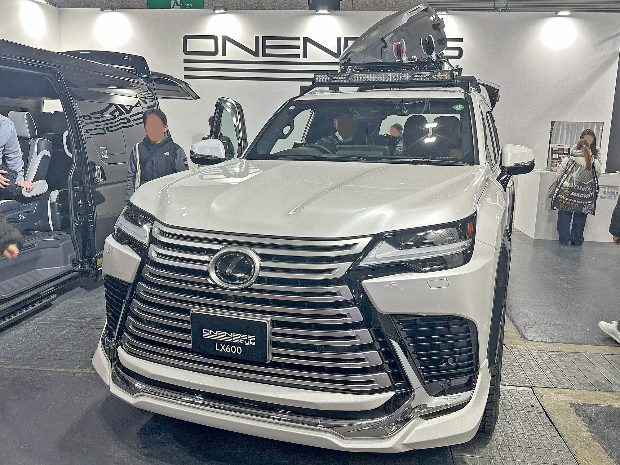 A white Lexus LX 600 built up with a roof rack, light bar and roof box on a show stand