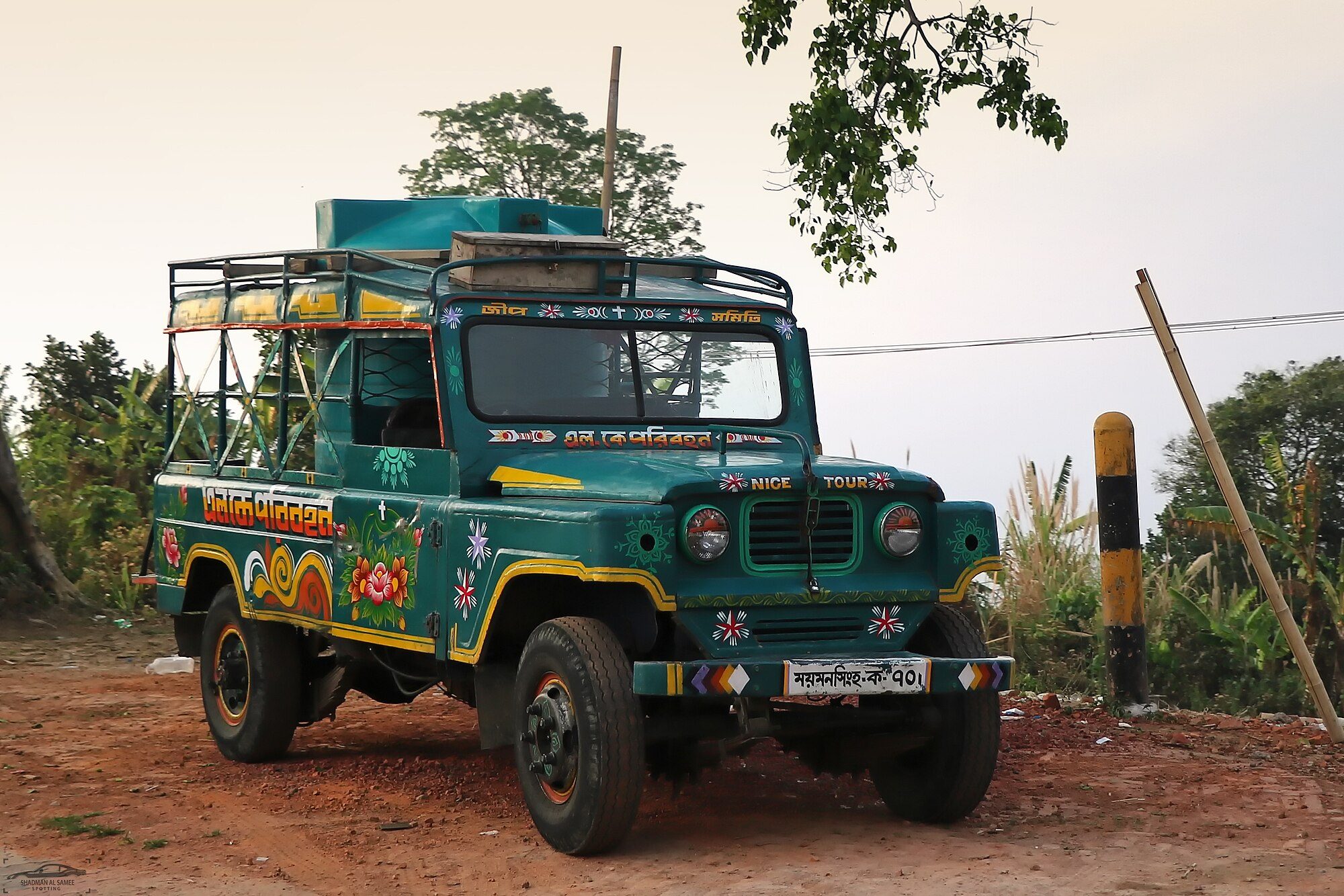 A hand-painted green Nissan Patrol 60 Chander Gari with a roof rack and water tank parked on red dirt among trees
