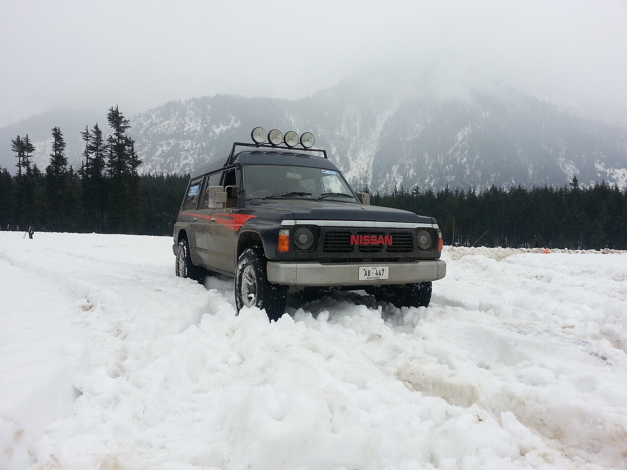 A black Y60 Patrol with roof-mounted spotlights parked in deep snow below forested mountains at Kalam, Swat, Pakistan