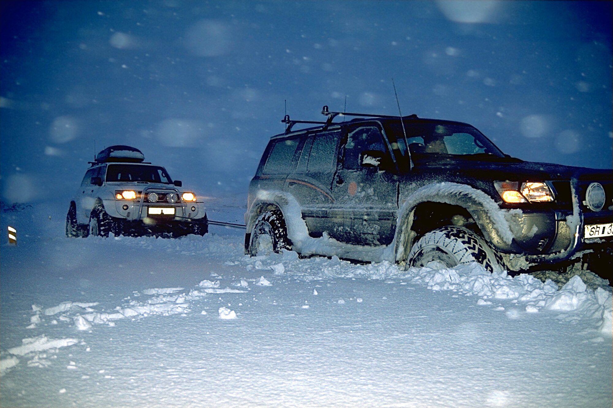 Two Nissan Patrol Y61s on big tyres, one towing the other through deep snow in Iceland