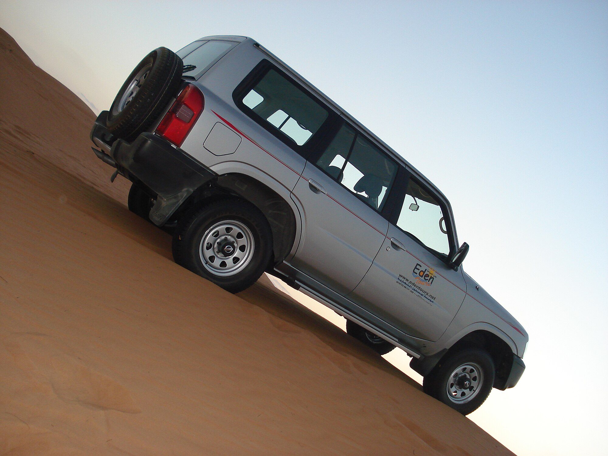 A silver facelifted Nissan Patrol Y61 wagon climbing a steep sand dune in Oman